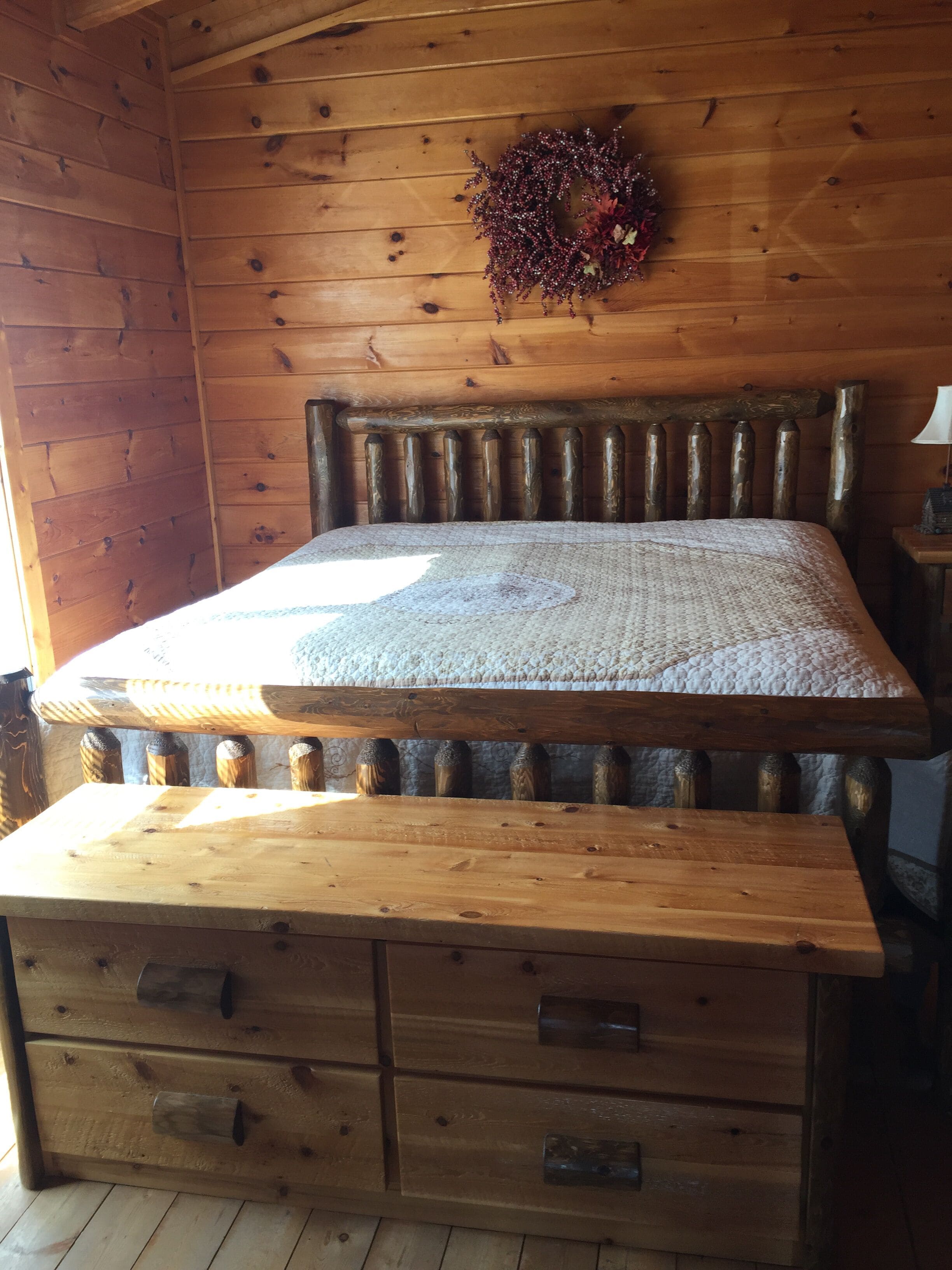 A wooden cabin room with a bed, a wooden dresser, and a decorative wreath on the wall.
