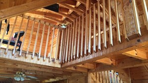 Un interior de madera con balcón, ventilador de techo y una silla negra.