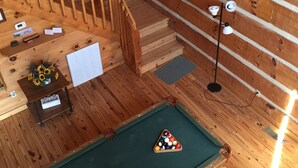 Un interior de madera con mesa de billar, una escalera y un cuadro en la pared.