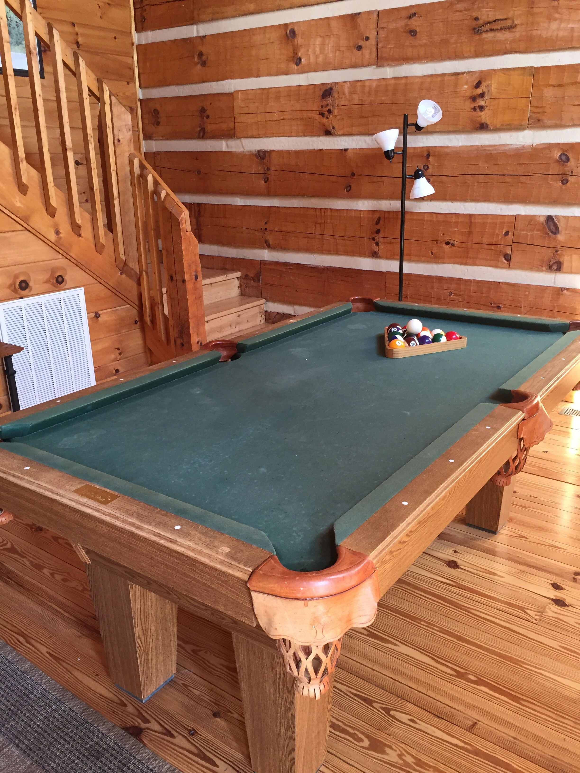 Une table de billard avec des billes, un escalier en bois et un mur fait de rondins de bois.