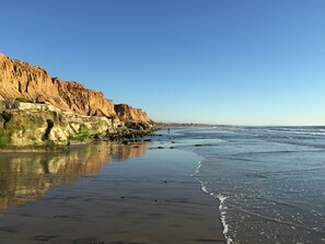 Una playa con un acantilado rocoso y olas tranquilas.