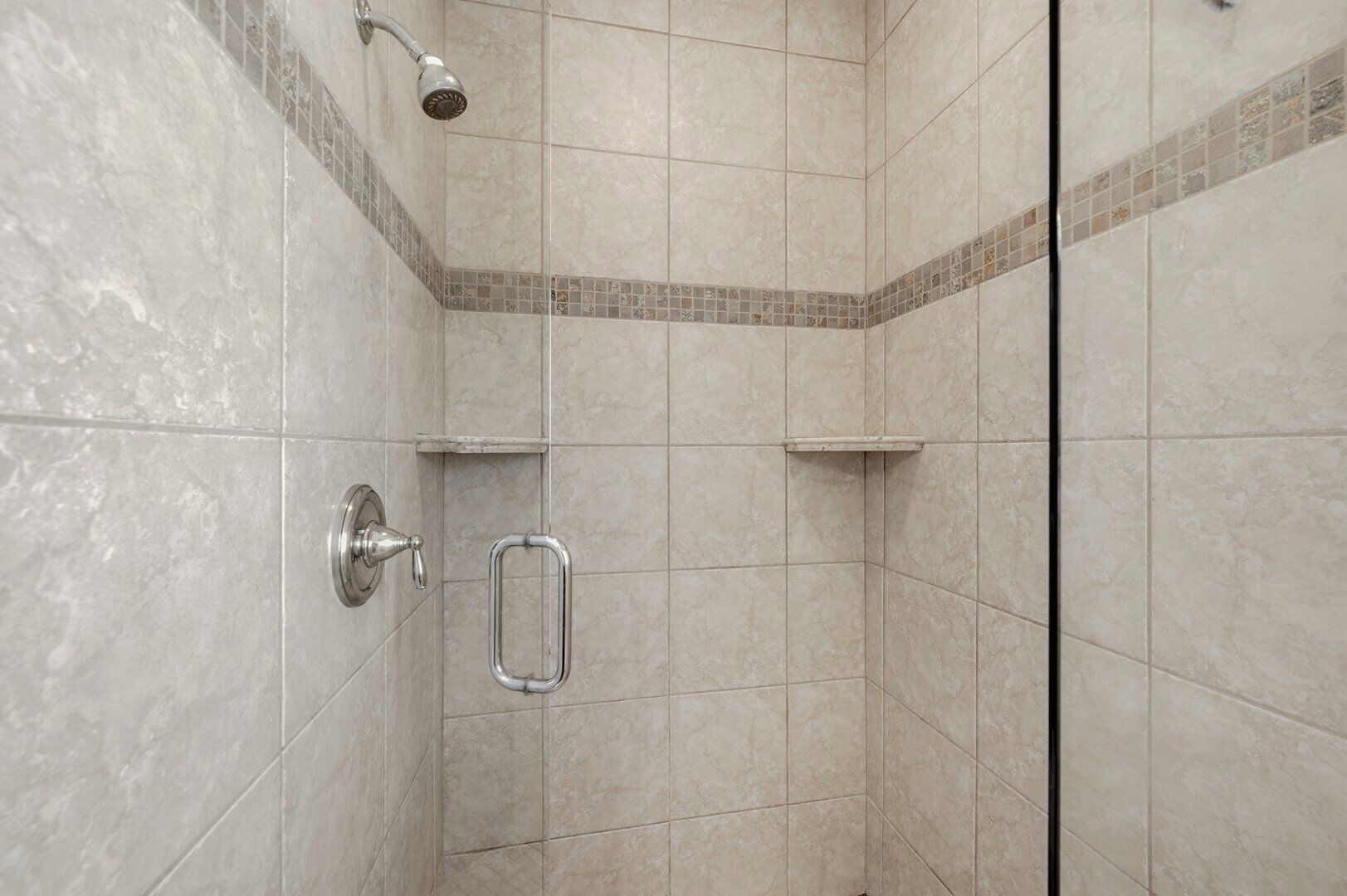 Zona de ducha con paredes de azulejos, ducha de mano, barra de apoyo y repisa.