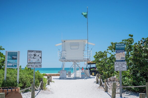 A lifeguard tower at a beach with signs about beach access, sea turtle safety, and a no-pets policy.