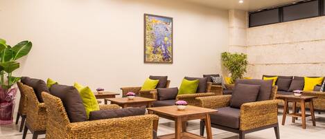 A modern lounge area with wicker furniture, wooden tables, and a large abstract painting on the wall.
