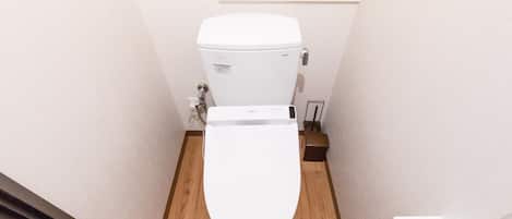 Un baño pequeño y funcional con inodoro blanco, suelo de madera y pared blanca.