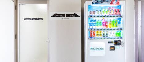 A vending machine with a variety of drinks and a sign indicating directions to rooms 301-310 and 311-320.
