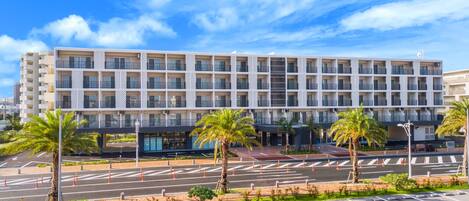 A modern hotel with a multi-story structure, a parking lot, and palm trees.