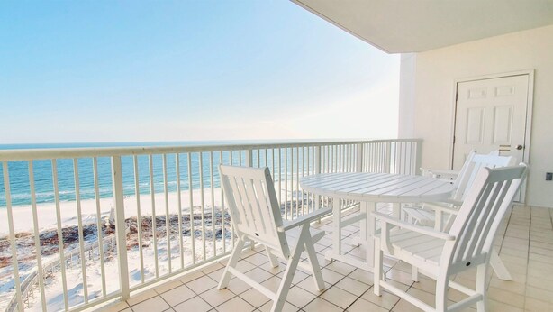 Ein Balkon mit weißem Tisch und Stühlen, der auf einen Strand mit freiem Blick auf das Meer blickt.