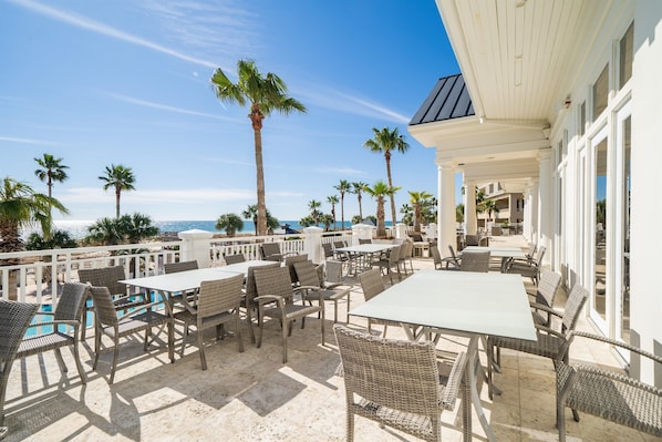 Une terrasse extérieure avec des tables et des chaises, des palmiers et une vue sur l’océan.