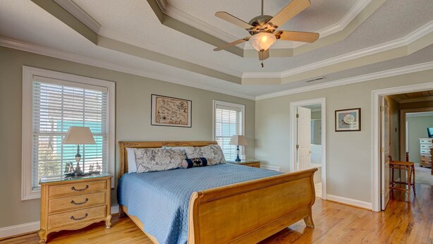 A bedroom with a wooden bed, two bedside tables, a ceiling fan, and a window with blinds.