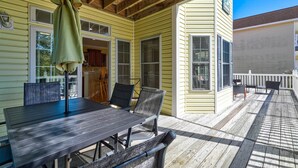 A covered patio with a table and chairs, wooden deck, and a view of the house.