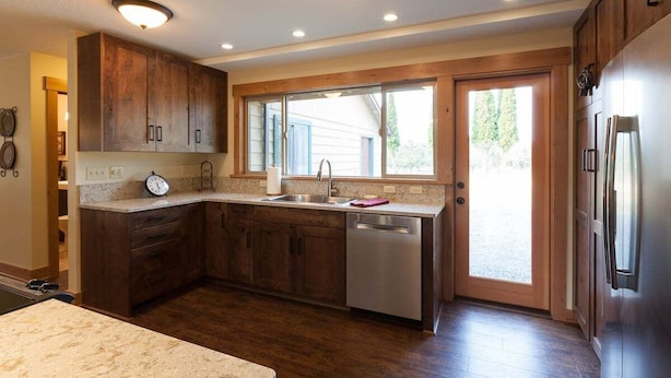 Una cocina con armarios de madera, un refrigerador de acero inoxidable, un lavavajillas y una ventana con vistas al exterior.