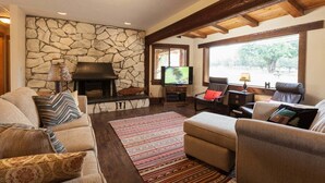 Una sala de estar acogedora con pared de piedra, chimenea, asientos cómodos y televisión.