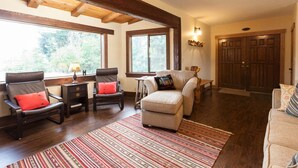Una sala de estar con chimenea, vigas de madera, un ventanal grande y una puerta.