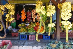 Un puesto de frutas con plátanos, manzanas, naranjas y piñas expuestas en cestas y cajas.
