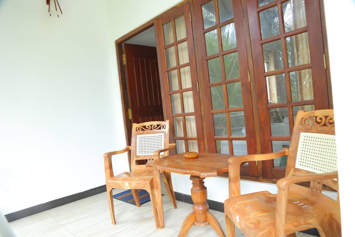 A room with a wooden table and four chairs, a large window with curtains, and a door leading outside.
