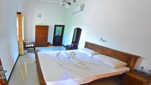 A hotel room with a large bed, wooden headboard, a ceiling fan, an air conditioning unit, a wooden wardrobe, and a small table with a chair. - Osanda Guest (Bentota)