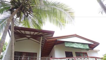 Un edificio de dos pisos con balcón, patio cubierto y una palmera.
