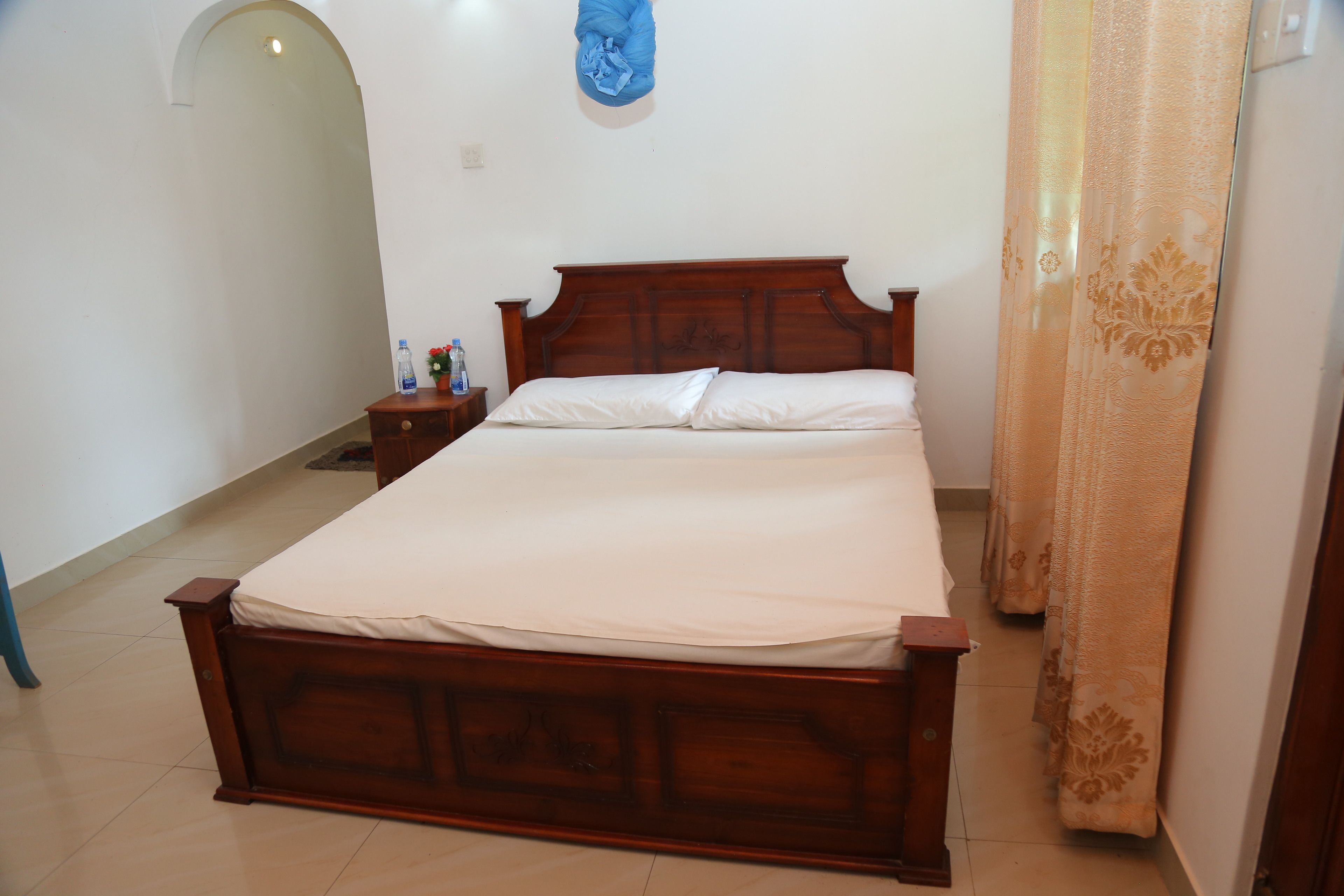 Un dormitorio con una cama de madera, una mesita de noche, una botella de agua y un paño azul colgado en la pared.