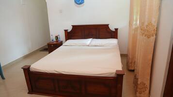 Un dormitorio con una cama de madera, una mesita de noche, una botella de agua y un paño azul colgado en la pared.