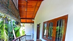 A covered outdoor seating area with wooden chairs and a table, a wooden railing, and a view of the surrounding greenery. - Osanda Guest (Bentota)