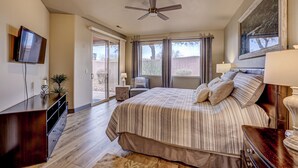 Ein Schlafzimmer mit Bett, Deckenventilator, Fernseher, Schreibtisch und Fenster mit Vorhängen.