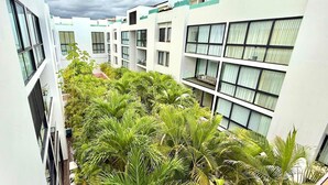 Een hotel met meerdere verdiepingen, balkons, een centrale binnenplaats met palmbomen en een heldere lucht.