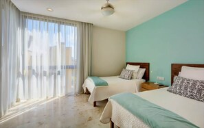 A hotel room with two beds, a large window with sheer curtains, a ceiling fan, and a view of the outside. - Central 2BR, Balcony, Gym, Pool, Garage (Playa del Carmen)
