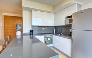 A modern kitchen with white cabinets, stainless steel appliances, a water dispenser, and a dining area with a long table and chairs.