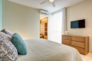 A bedroom with a bed, a TV, a wooden dresser, and a walk-in closet.