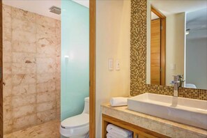 A bathroom with a marble shower wall, a toilet, a sink with a mosaic backsplash, and a mirror. - Central 2BR, Balcony, Gym, Pool, Garage (Playa del Carmen)