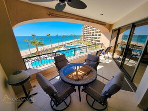 Varanda com vista para a praia e piscina. Há quatro cadeiras e uma mesa.