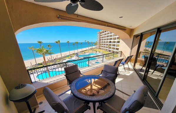 Un balcon avec vue sur une plage et une piscine. Il y a quatre chaises et une table.