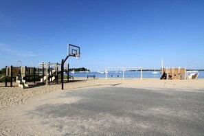 Una spiaggia con un campo da basket, un'area giochi e vista sul mare.