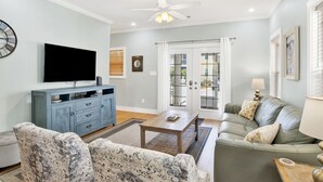 Ein Wohnzimmer mit Flachbildfernseher, blauem Schrank, gemustertem Sofa und einem grünen Couch mit Kissen.