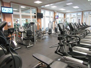 A gym with various exercise machines, mirrors, and large windows.