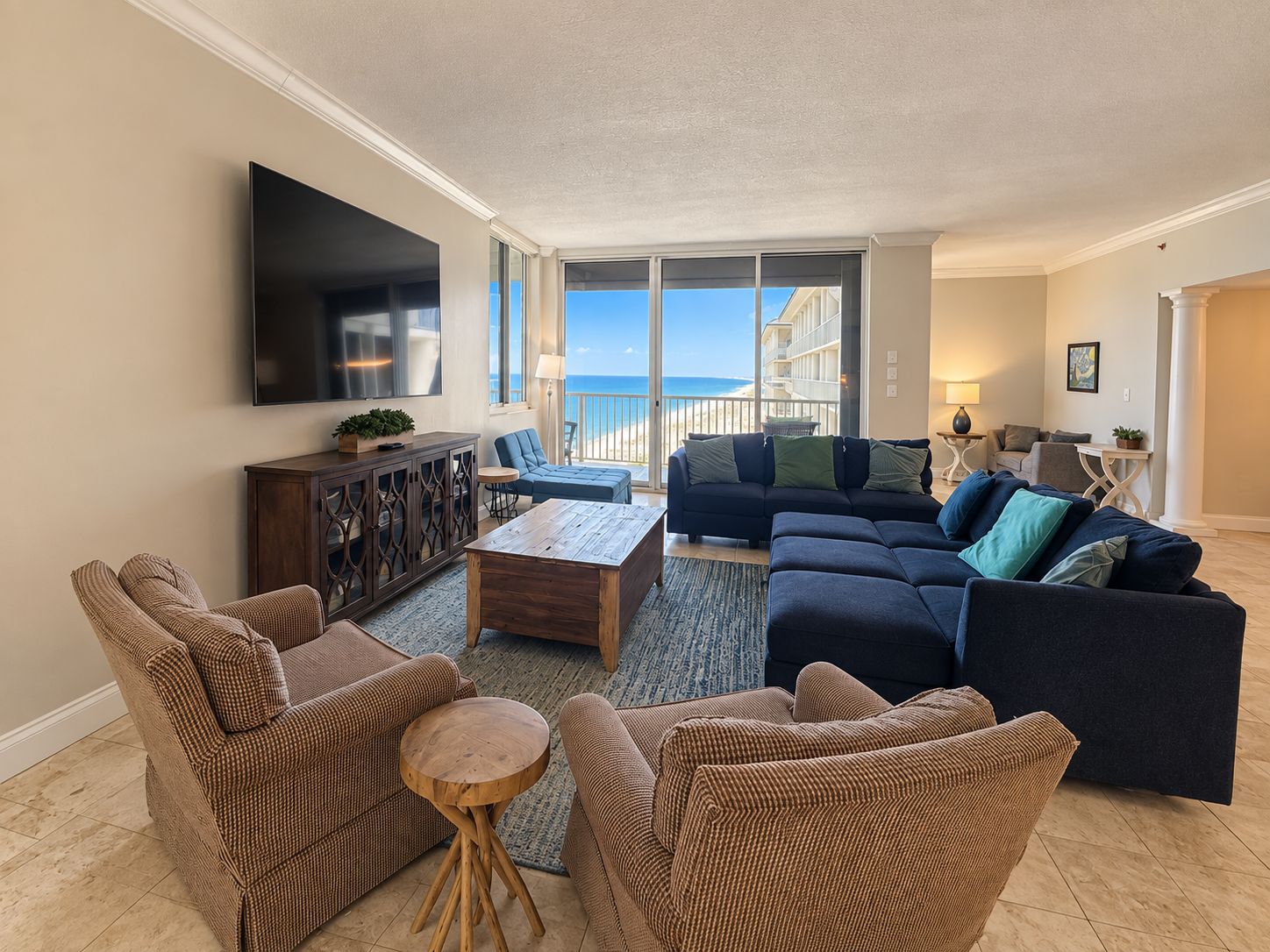 A living room with a large TV, a sofa set, a coffee table, and a view of the ocean.