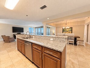 A spacious kitchen with a granite countertop, wooden cabinets, and a dining area with a white table and chairs. - Beach Club Avalon Penthouse 2003 Direct Gulf Views/5 Kings Total Renovation! (Gulf Shores)