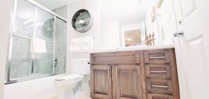 A bathroom with a glass shower enclosure, a white toilet, and wooden cabinets.