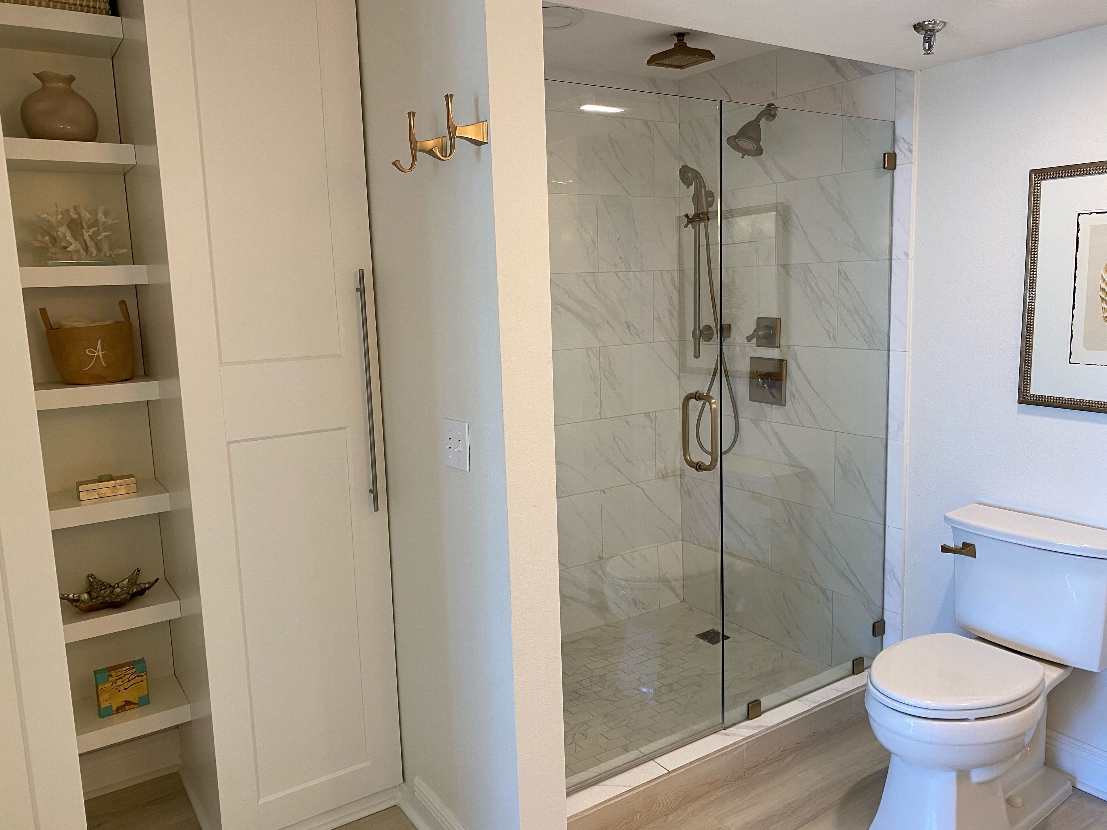 Un baño con ducha envuelta en vidrio, un inodoro y un mueble con adornos.