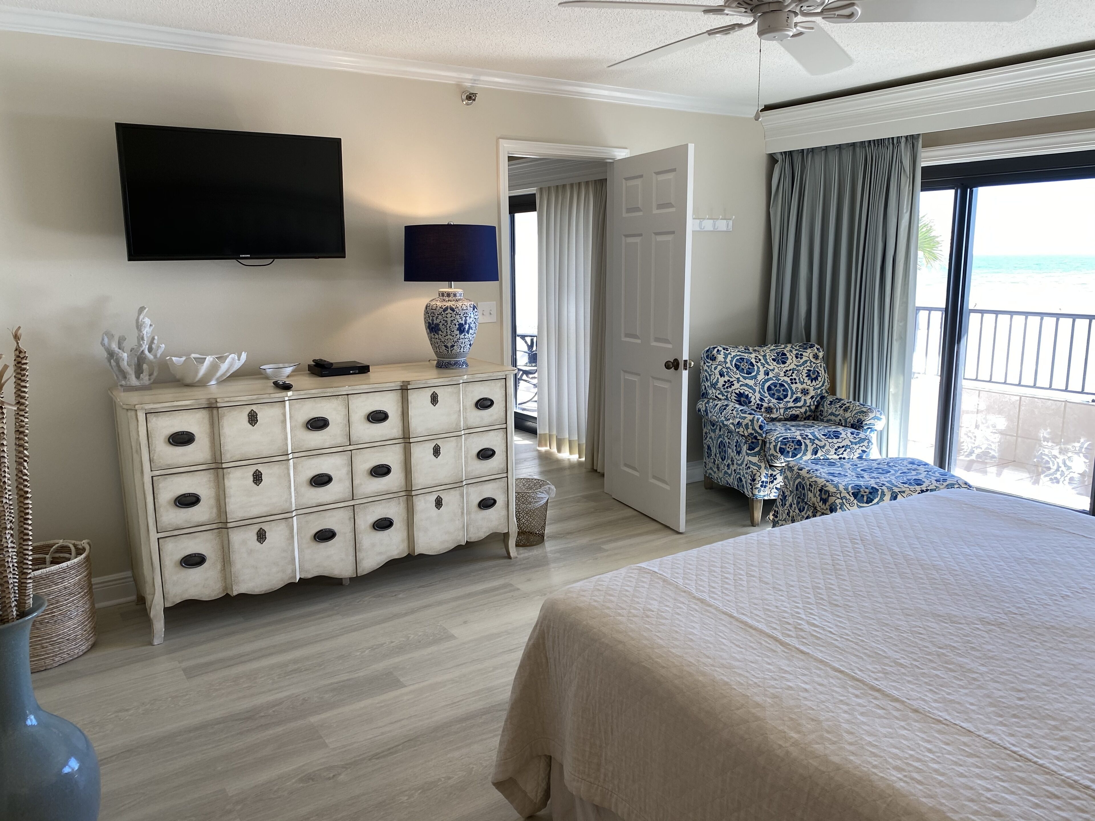 A hotel room with a bed, a dresser, a TV, a chair, and a balcony with a view.