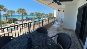 A balcony with a pool view, white rocking chairs, and a table with a vase.