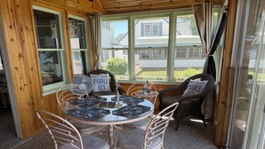 A cozy room with a round table, four chairs, and a view of a house through large windows. - Diamond Lake Island Cabin   (Cassopolis)