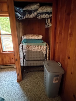 A compact room with a bunk bed, a laundry basket, and a window with a view of greenery.