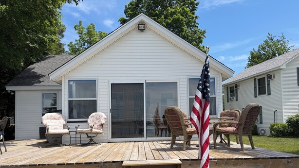 A house with a wooden deck, sliding glass doors, wicker chairs, and an American flag. - Diamond Lake Island Cabin   (Cassopolis)