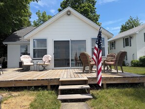 A house with a wooden deck, sliding glass doors, wicker chairs, and an American flag. - Diamond Lake Island Cabin   (Cassopolis)