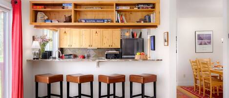 A modern kitchen with wooden cabinets, a built-in oven, and a bar area with stools.