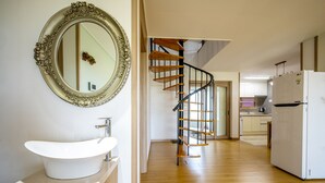 A modern kitchen with a white refrigerator, wooden flooring, and a spiral staircase leading to another level. - Jeju Blue & Sea (Seogwipo)