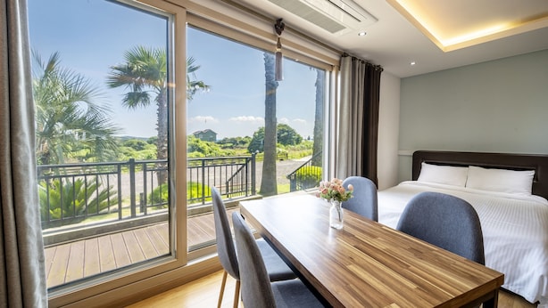 A hotel room with a balcony, a wooden table, and a bed with white bedding. - Jeju Blue & Sea (Seogwipo)