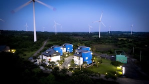 A residential area with multiple wind turbines in the background and a cluster of blue and white houses in the foreground. - Jeju Blue & Sea (Seogwipo)
